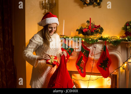 Portrait of young mother putting Christmas gifts in stockings hanging on fireplace Stock Photo