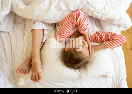 Portrait of little girl and sisters feet on pillow at bed Stock Photo