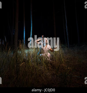 Young woman in nightgown sitting in high forest at night with lantern Stock Photo
