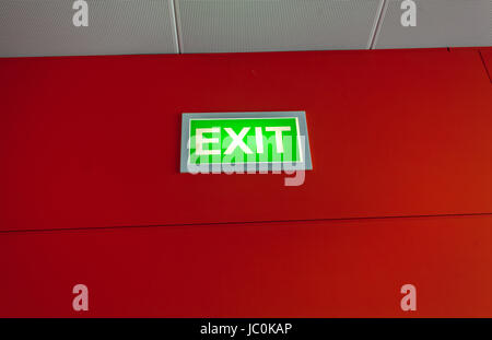 Green exit sign glowing on red wall Stock Photo