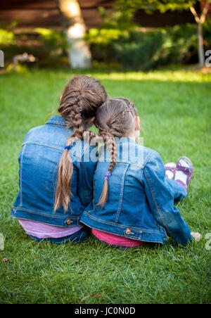 Two little sisters sitting on grass head to head with joint braids Stock Photo