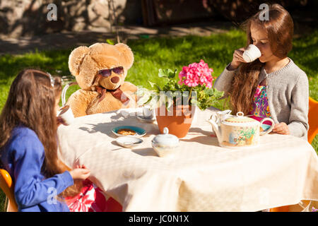 Two little sisters having english breakfast with teddy bear at yard Stock Photo