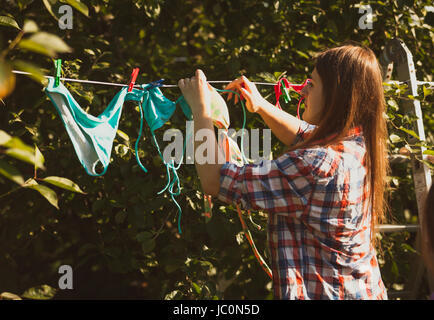 Toned photo of beautiful woman drying swimsuits on clothesline Stock Photo