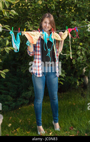 Beautiful woman hanging swimsuits on clothesline at garden Stock Photo