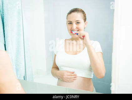 Portrait of young pregnant woman brushing teeth at bathroom Stock Photo