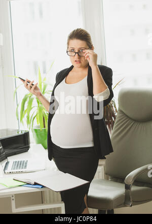 Portrait of pregnant businesswoman in black suit using mobile phone Stock Photo