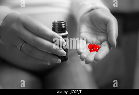 Closeup black and white photo of pregnant woman holding red pill on hand Stock Photo