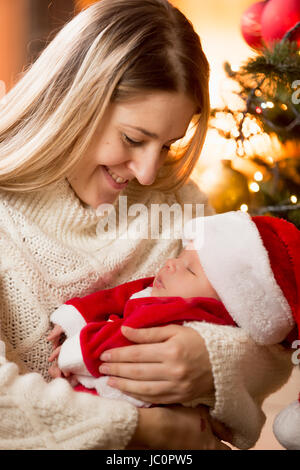 Happy young mother hugging baby boy in Santa costume at fireplace Stock Photo