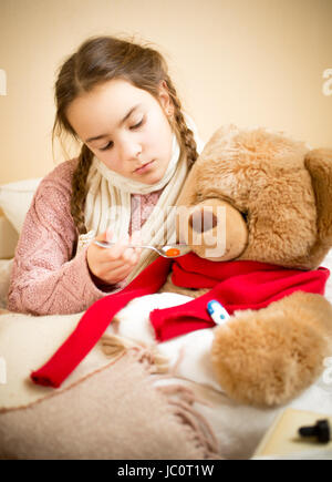 Portrait of little girl giving pills to sick teddy bear Stock Photo