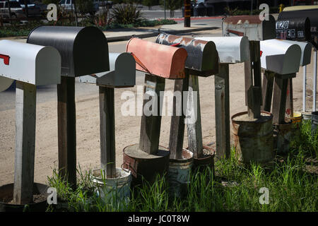 Row of individual mailboxes on posts set in cement cans along a rural road. Stock Photo