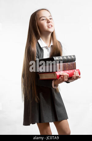 Portrait of schoolgirl carrying heavy stack of books against white background Stock Photo