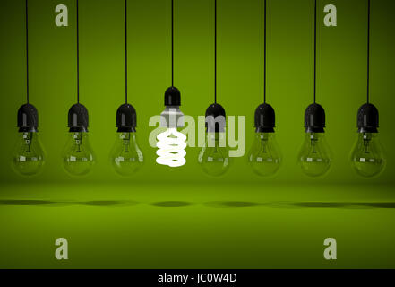 One glowing energy saving bulb in row of dark incandescent bulbs hanging on wires over green background Stock Photo