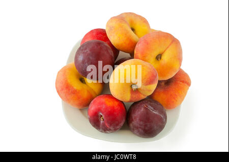 New variety of flat peaches and plums lying on white dish against a white background Stock Photo