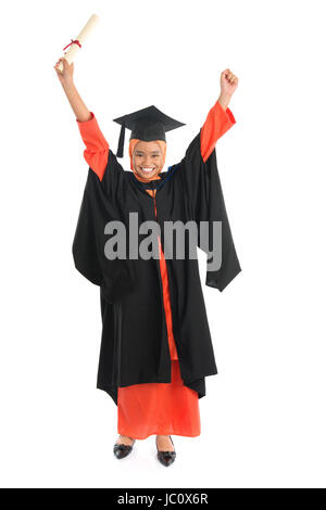 Portrait of full length smiling Asian female Muslim student in graduate gown hands raised showing graduation diploma standing isolated on white background. Stock Photo