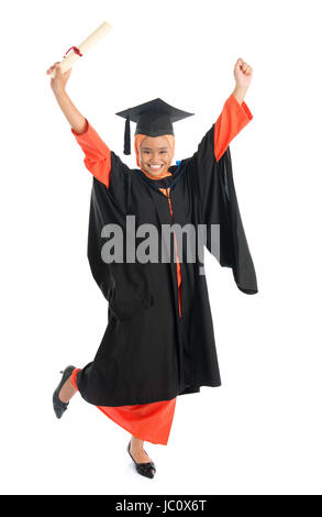 Portrait of full length smiling Asian female Muslim student in graduate gown hands raised showing graduation diploma jumping isolated on white background. Stock Photo