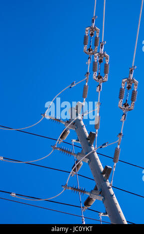 Right-angle junction of electrical power lines and insulators on pole against clear blue sky. Stock Photo