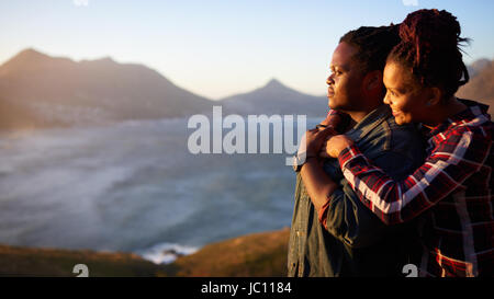 Interracial couple looking at the sunset ocean and mountain view Stock Photo