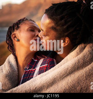 Close up mixed race couple kissing outdoors under a blanket Stock Photo