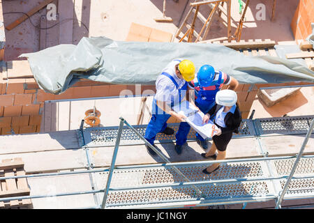 Construction site Team or architect and builder or worker with helmets discuss on a scaffold construction plan or blueprint or checklist Stock Photo