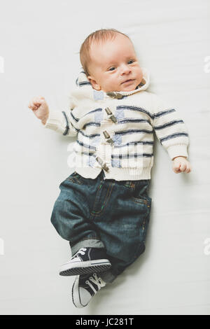 Toned photo of cute baby boy in jeans and sweater lying on bed Stock Photo