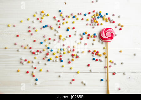 Lots of colorful little candies and big lollipop on white wooden background Stock Photo