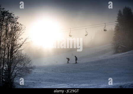 Beautiful silhouette photo of riding skiers and ski lift against bright winter sun Stock Photo