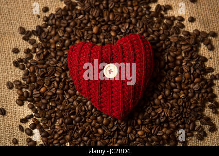 Closeup photo of knitted red heart lying on pile of coffee beans Stock Photo