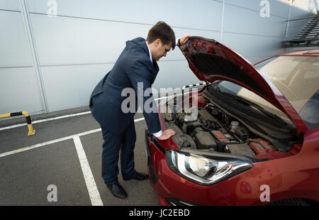 Stressed young businessman looking under the car hood Stock Photo