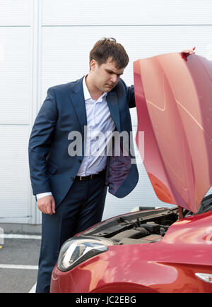 Handsome young man in suit looking under the hood of broken car Stock Photo