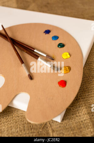 Three paintbrushes lying on wooden pallet with oil paint blobs Stock Photo