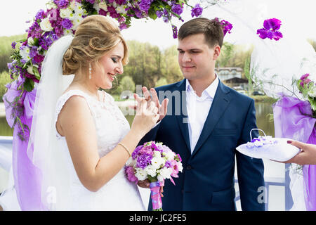 Portrait of happy bride putting golden ring on grooms hand at wedding ceremony Stock Photo