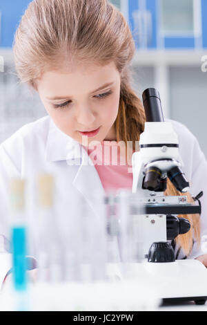 Concentrated little girl in white working with microscope in chemical lab Stock Photo