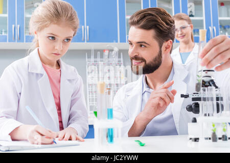 Smiling bearded teacher and serious little student making experiment in lab Stock Photo