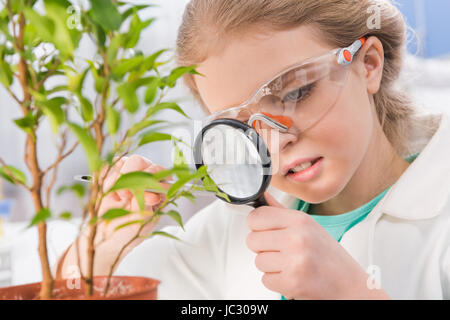 adorable little girl in goggles with magnifying glass and plant in laboratory Stock Photo