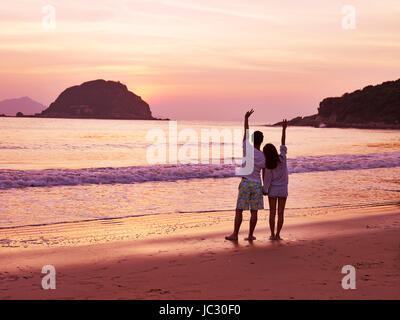 young asian couple taking a walk on beautiful beach before sunrise. Stock Photo