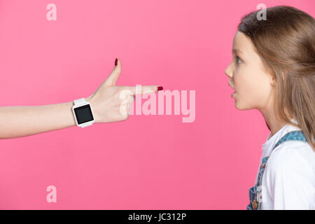 Side view of shocked little girl looking at woman with smartwatch pointing with finger Stock Photo