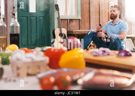 Handsome bearded young man sitting on porch and drinking beer Stock Photo