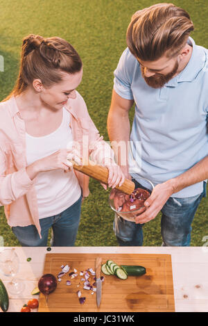 High angle view of young couple pouring spices in meat for barbecue Stock Photo
