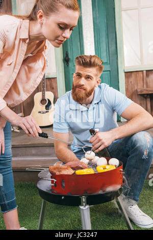 man and woman roasting meat and vegetables on barbecue grill Stock Photo