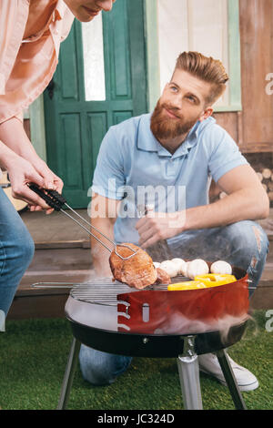 man and woman roasting meat and vegetables on barbecue grill Stock Photo