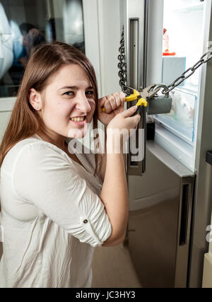 Portrait of angry woman cutting chain on refrigerator with cutters Stock Photo
