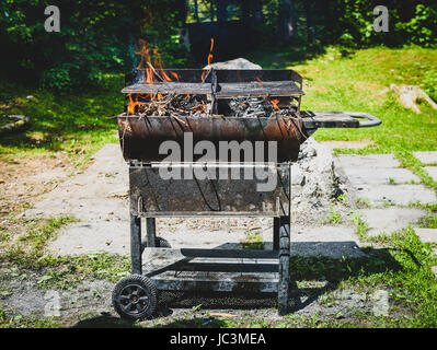 Burning and preheating old rusty barbecue grill cleaning dirty grid. Flames in bbq in nature - outdoors picnic. Preparing the barbecue for charcoal on Stock Photo