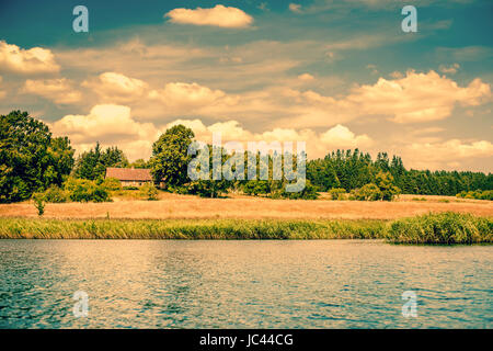 House by a riverside surrounded by fields and trees Stock Photo