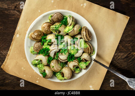 An overhead photo of escargots a la bourguignonne, a plate of snails with the typical French green sauce of garlic and herb butter, on a rustic textur Stock Photo