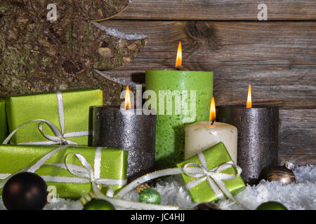 Christmas decoration: four red and brown burning advent candles with gift boxes and snowy wooden background. Stock Photo