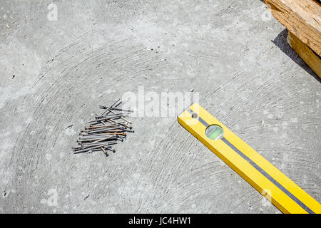 Nails are lying down on clean concrete background. Bubble spirit level is used to control concrete surface. Stock Photo