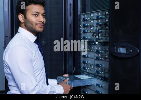 Data security. Handsome delighted bearded man standing near the network server and installing the blade server in it while doing his job Stock Photo