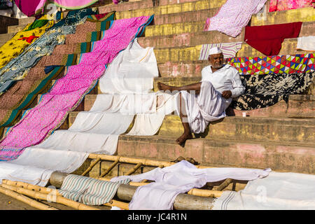 A man is sitting on the stairs, surrounded by drying laundry at the holy river Ganges at Dashashwamedh Ghat, Main Ghat, in the suburb Godowlia Stock Photo