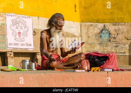 A Sadhu, holy man, is sitting on a platform and studying religious skriptures at the holy river Ganges at Meer Ghat in the suburb Godowlia Stock Photo