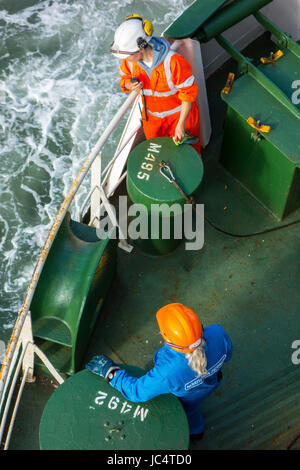 Male and female crew member in orange and blue overalls and wearing safety helmets working on deck of ferry boat Stock Photo
